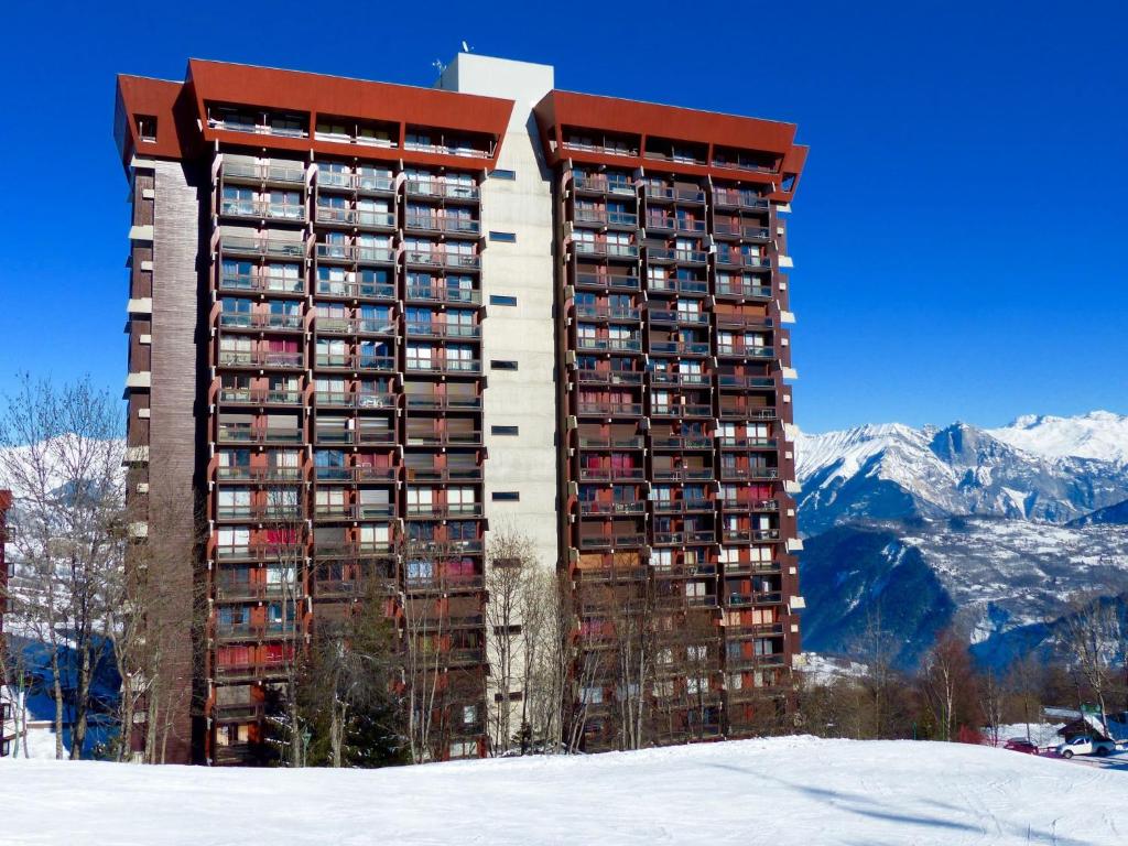 un grand immeuble dans la neige avec des montagnes dans l'établissement Studio Lunik Orion-49 by Interhome, au Corbier