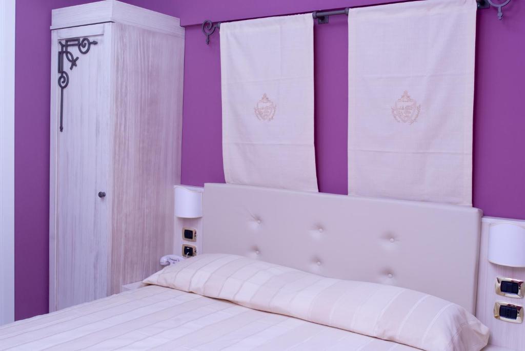 - un lit blanc aux murs violets et aux rideaux blancs dans l'établissement Palazzo Reginella, à Bovalino Marina