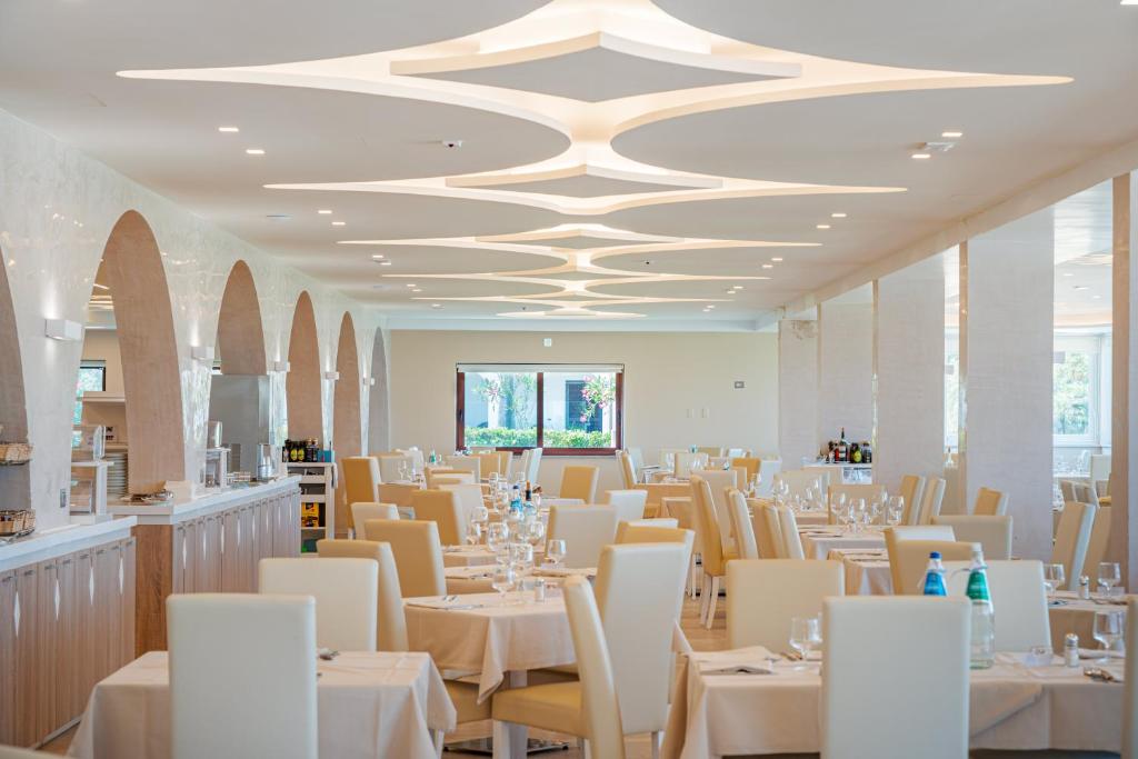 une salle à manger avec des tables blanches et des chaises blanches dans l'établissement Hotel Portoconte, à Porto Conte