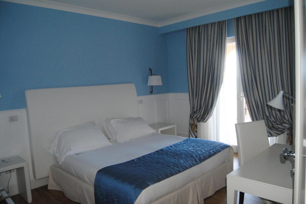 une chambre avec un lit aux murs bleus et une fenêtre dans l'établissement Helios Hotel, à Crotone
