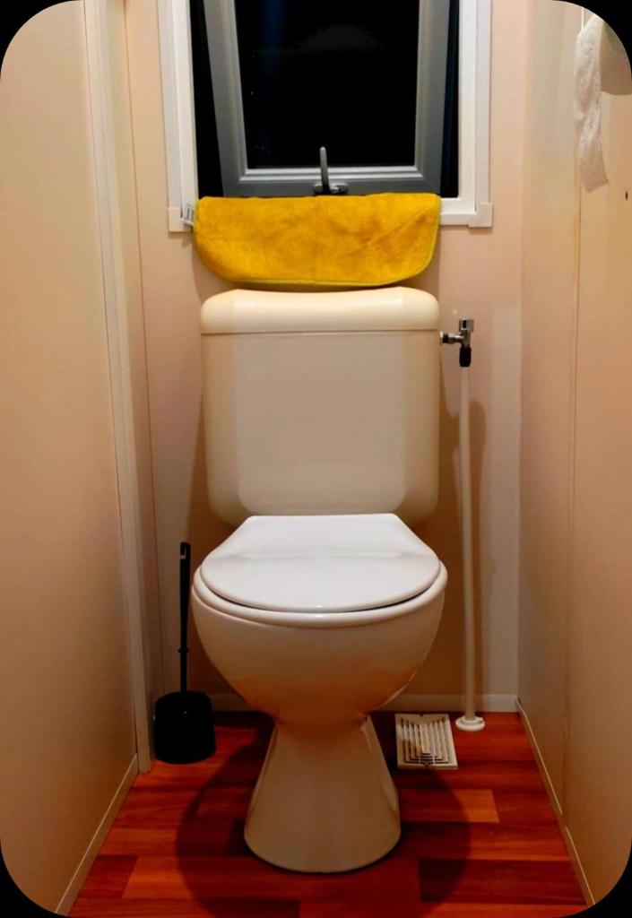 La salle de bains est pourvue de toilettes, d'une fenêtre et d'une serviette jaune. dans l'établissement Mobil Home près de l'entrée et de la piscine, à Saint-Chéron 10 autres photos