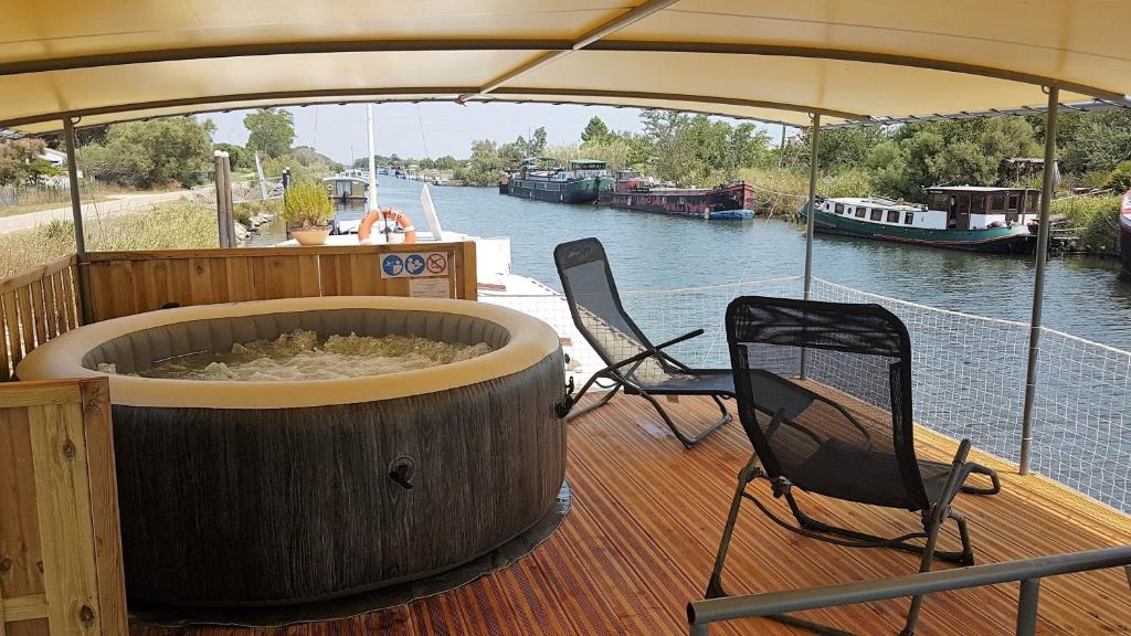 une terrasse en bois avec deux chaises et une grande baignoire sur un bateau dans l'établissement PÉNICHE authentique tout confort, à Aigues-Mortes