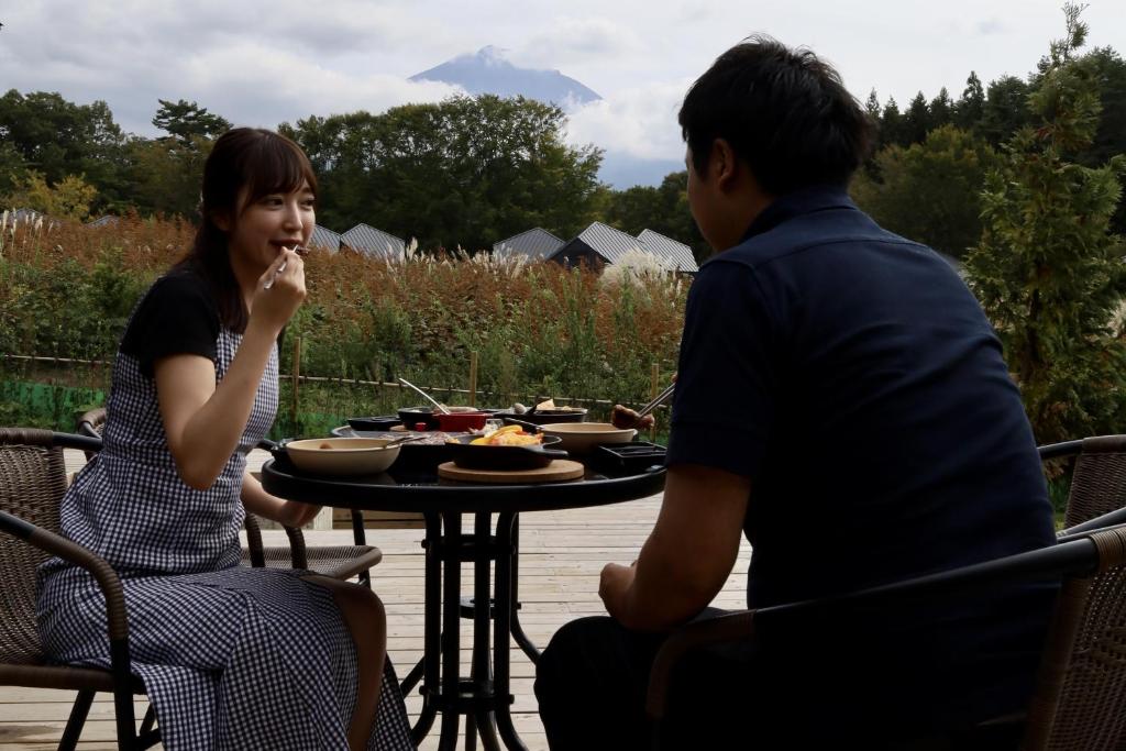 un homme et une femme assis à une table avec de la nourriture dans l'établissement グランピングヴィレッジ富士河口湖, à Narusawa