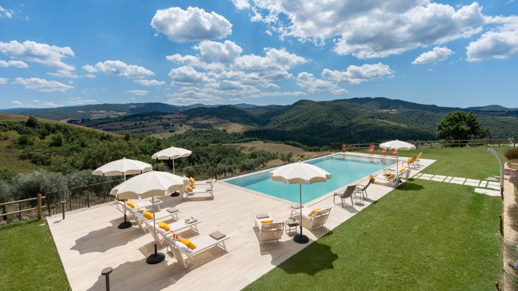 - une piscine avec des chaises et des parasols sur une terrasse avec des montagnes dans l'établissement CASOLARE SAN MARTINO 16&1, Emma Villas, à Pomarance