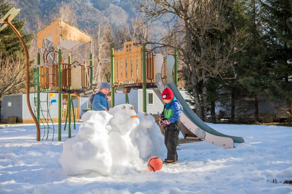deux enfants jouant avec un bonhomme de neige sur une aire de jeux dans l'établissement Camping RCN Belledonne, au Bourg-dʼOisans