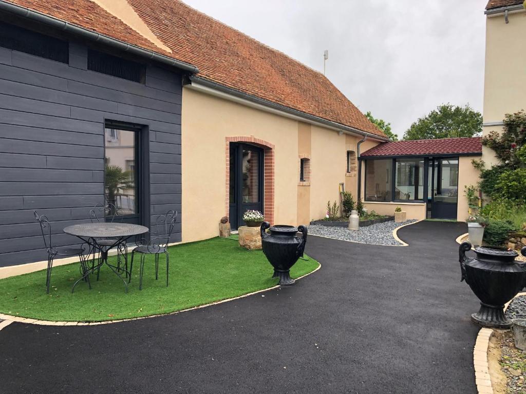 une cour avec une table et des chaises à côté d'un bâtiment dans l'établissement Gîte Confortable près du Mans avec Piscine, Parc de Jeux et Vélo - FR-1-410-364, à Louplande