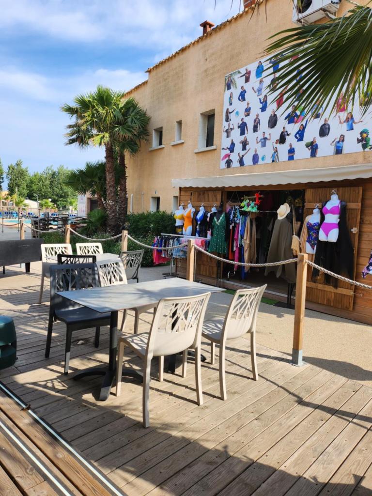 une table et des chaises sur une terrasse en bois avec un magasin dans l'établissement FMLODGE-mobilhome jasmin, à Valras-Plage