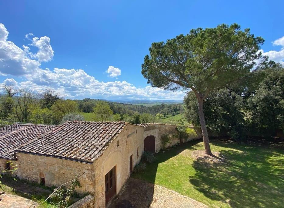un vieux bâtiment avec un arbre dans un champ dans l'établissement Tenuta Uzielli an elegant countryside villa, à Monteriggioni