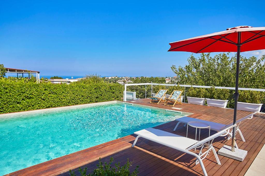 - une piscine avec un parasol rouge, 2 chaises et une table avec un parasol dans l'établissement Villa Ametista, à Alcamo