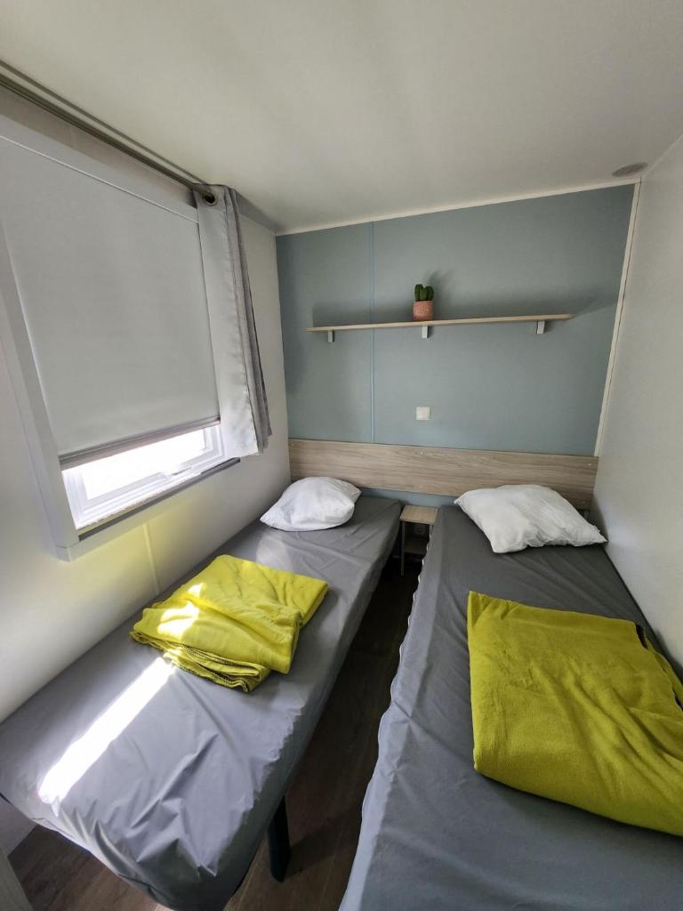 deux lits dans une petite pièce avec une fenêtre dans l'établissement Mobil-home cosy 166, à Narbonne