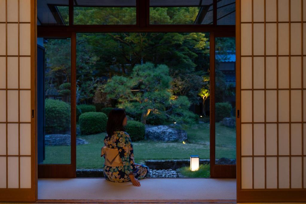 une femme qui regarde un jardin par une fenêtre dans l'établissement Tokiwa Bekkan, à Toyooka