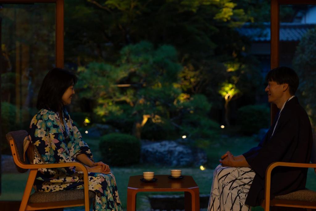 un homme et une femme assis sur des chaises devant un jardin dans l'établissement Tokiwa Bekkan, à Toyooka 16 autres photos