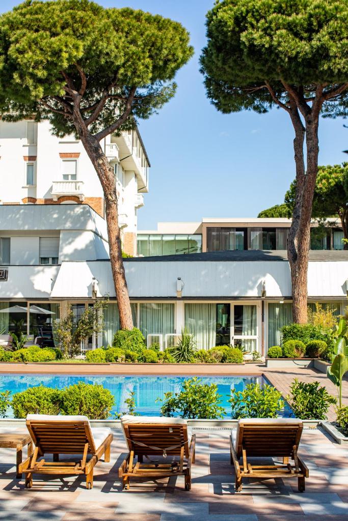 un complexe avec deux chaises et une piscine dans l'établissement Villa Regina - MarePineta Resort, à Milano Marittima