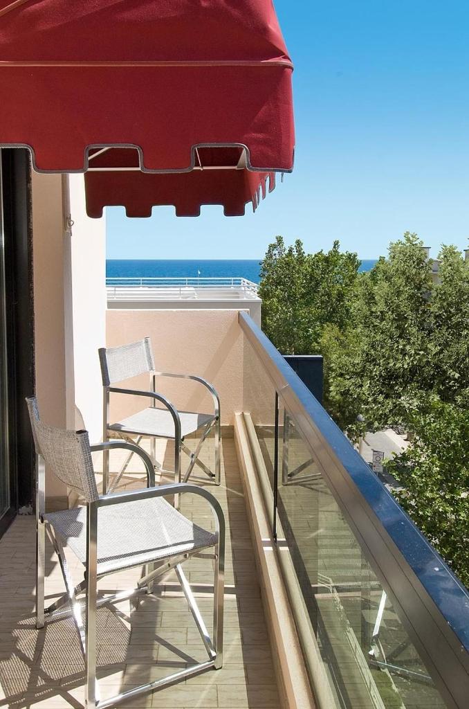 - un balcon avec 2 chaises et un parasol rouge dans l'établissement Hotel Novella, à Misano Adriatico