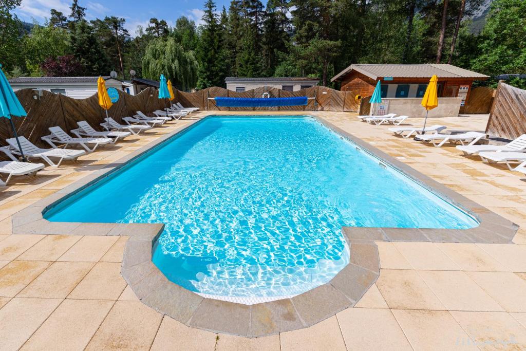 une grande piscine bleue avec chaises et parasols dans l'établissement Mobil Home XXL 4 chambres - Camping Les Relarguiers, à Beauvezer