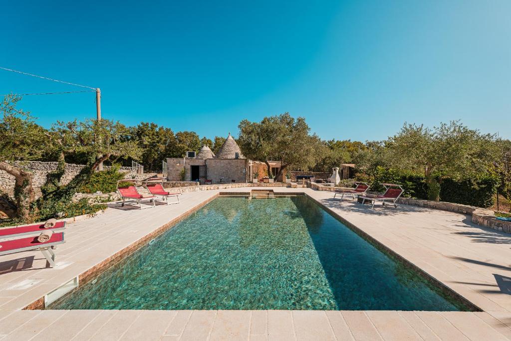 une piscine avec des chaises et un bâtiment dans l'établissement HelloApulia Trulli Serena, à Alberobello
