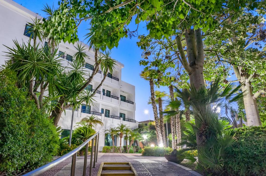 une passerelle devant un bâtiment blanc avec des arbres dans l'établissement Acacia Marina, à Marina di Ragusa