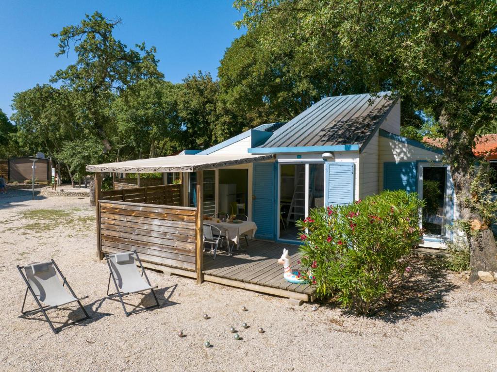 une petite maison avec deux chaises et une terrasse dans l'établissement Camping Le Bois Fleuri, à Argelès-sur-Mer