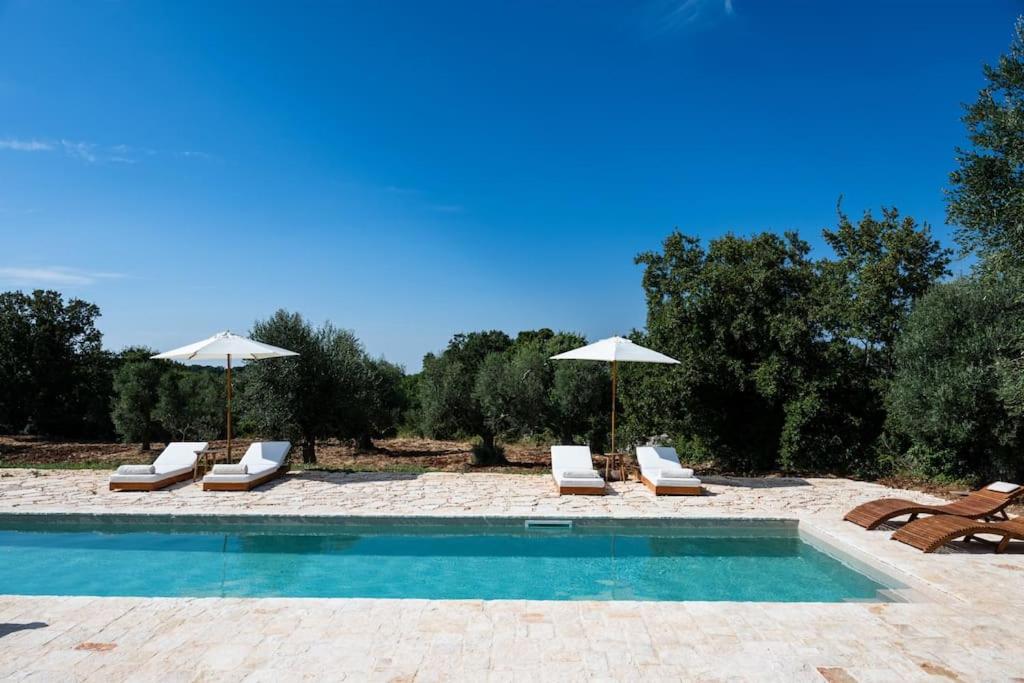 une piscine avec chaises longues et parasols dans l'établissement Trullo Elaia - Dimora di charme in Valle d'Itria con piscina, à Ceglie Messapica