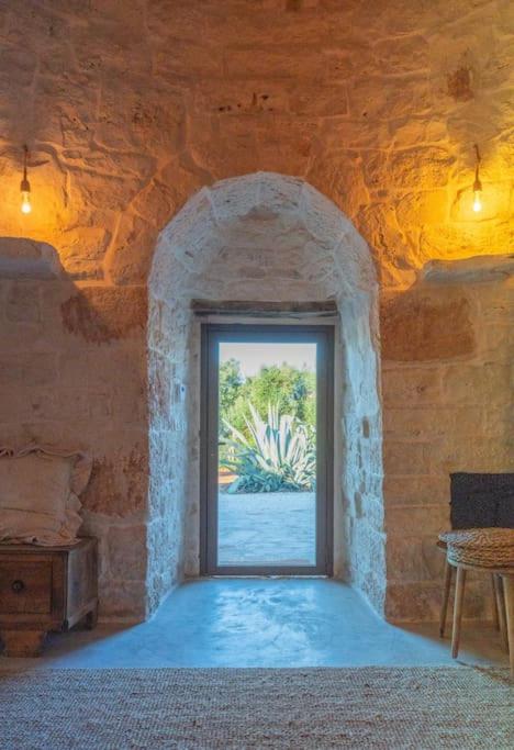 Cette chambre est dotée d'une porte ouverte dans un mur en pierre. dans l'établissement Trullo Elaia - Dimora di charme in Valle d'Itria con piscina, à Ceglie Messapica 92 autres photos