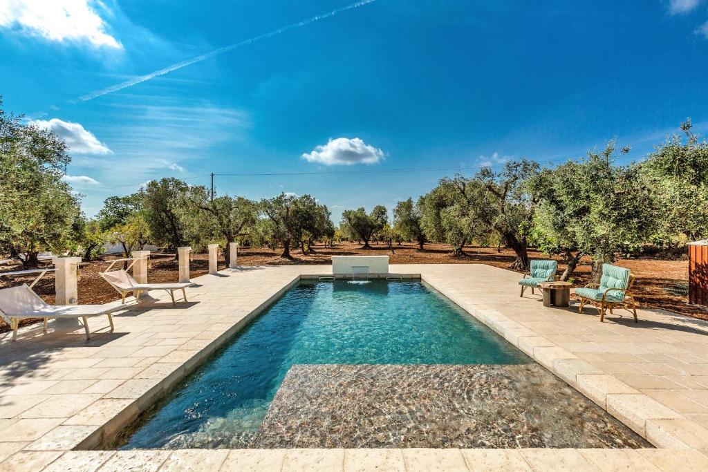 - une piscine avec 2 chaises et une table à côté dans l'établissement Trullo Antica Puglia by Perle di Puglia, à San Michele Salentino