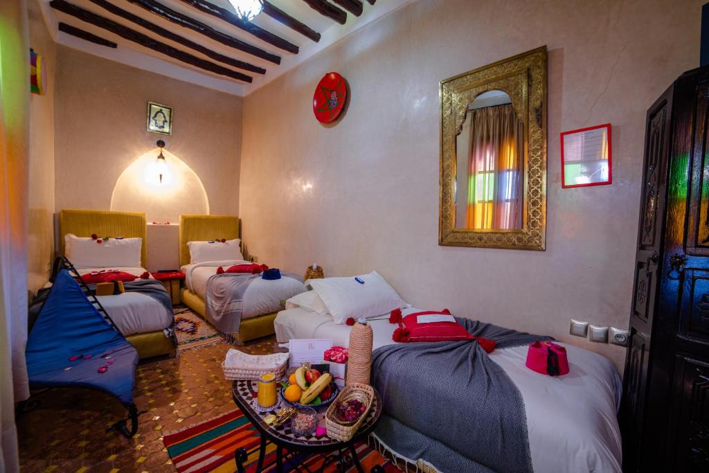 Cette chambre comprend 3 lits, une table et un miroir. dans l'établissement Riad Eva, à Marrakech