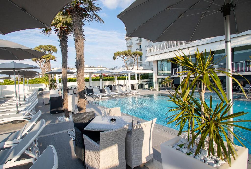une piscine de villégiature avec des chaises blanches et un parasol dans l'établissement Hotel Sayonara, à Lido di Jesolo