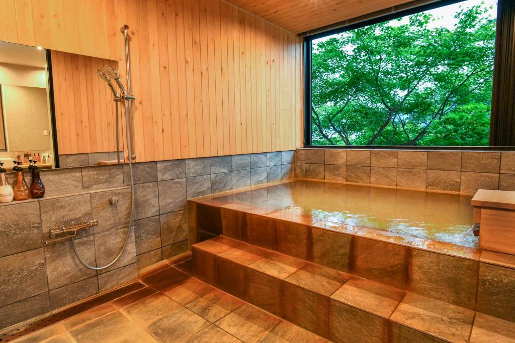 La salle de bains est pourvue d'une grande baignoire et d'une fenêtre. dans l'établissement Sozankyo, à Aso