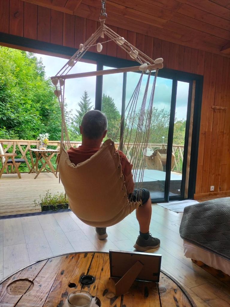 un homme assis dans un hamac dans une pièce dans l'établissement Cabane perchée avec jacuzzi, à La Roche-Maurice