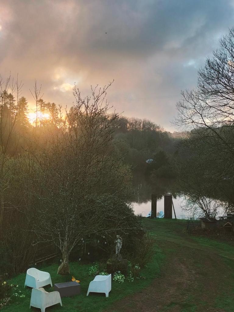 Deux bancs blancs assis dans l'herbe près d'un lac dans l'établissement Cabane perchée avec jacuzzi, à La Roche-Maurice