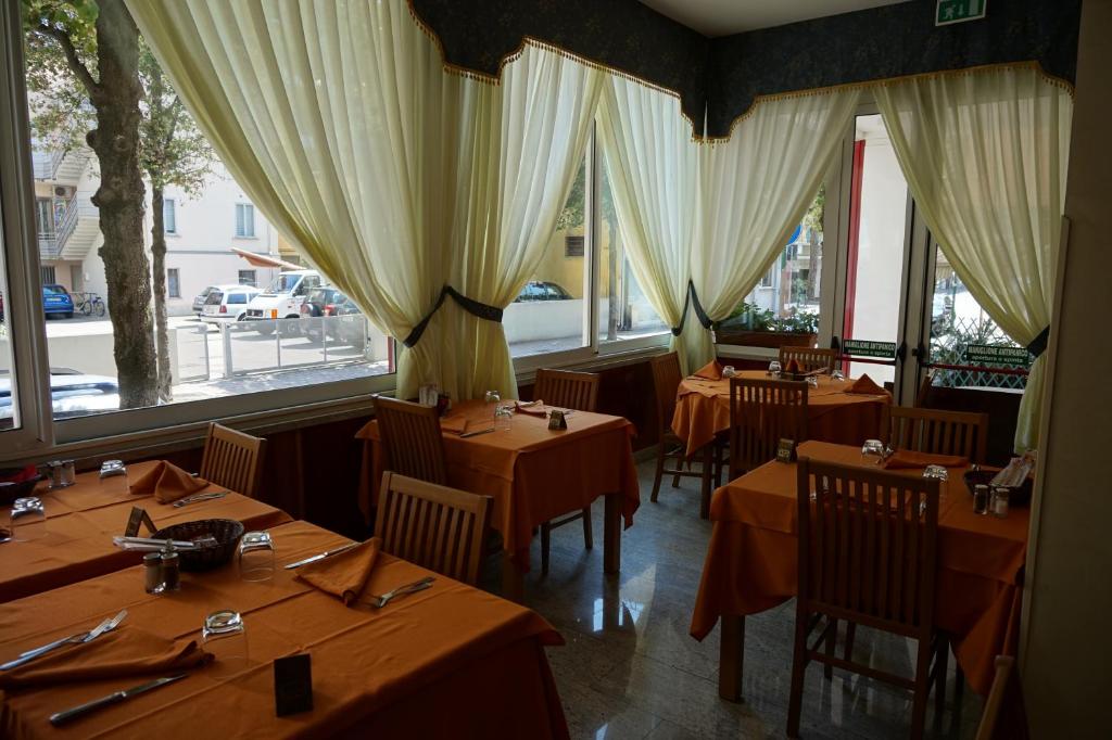 une rangée de tables dans un restaurant avec fenêtres dans l'établissement Hotel Flora, à Lignano Sabbiadoro