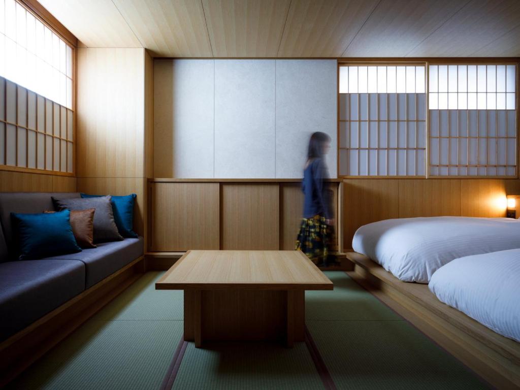 une femme dans une chambre avec deux lits et une table dans l'établissement 黒梅屋 Kurumiya, à Kanazawa