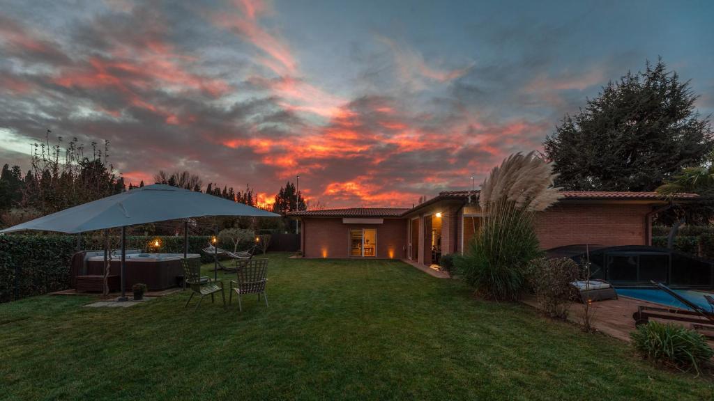 une maison avec un parasol dans la cour au coucher du soleil dans l'établissement VILLA VIVI' 8, Emma Villas, à Monte San Savino