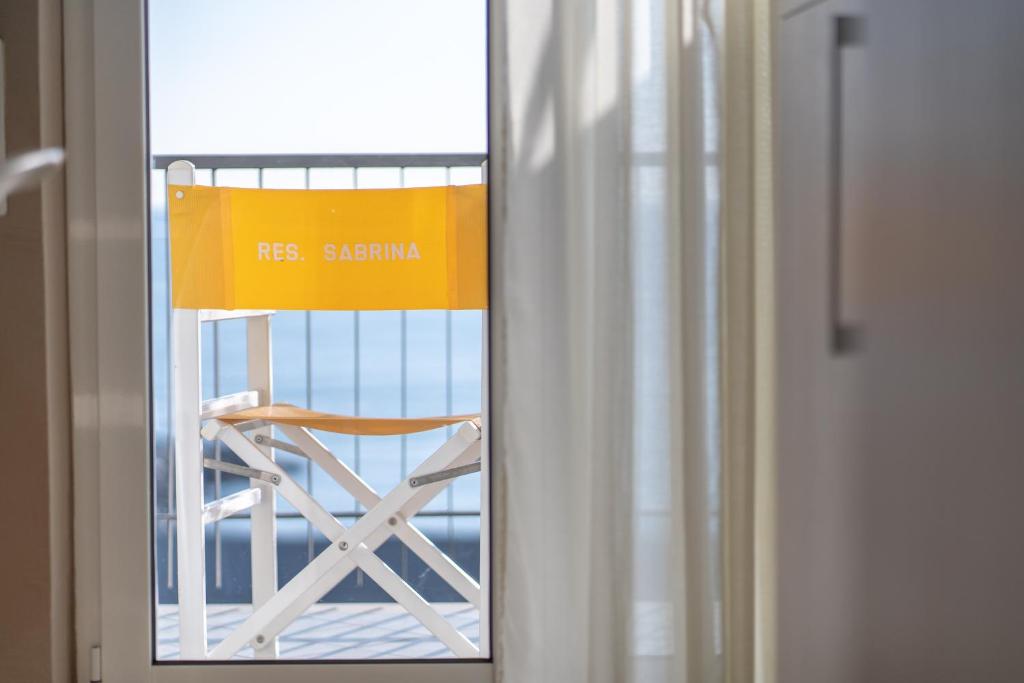 un panneau jaune assis sur une chaise dans une fenêtre dans l'établissement Residence Sabrina, à Ceriale