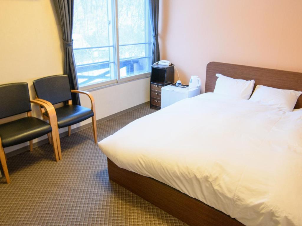 une chambre avec un lit et deux chaises et une fenêtre dans l'établissement Ryokan HANAEMI, à Otaru 13 autres photos