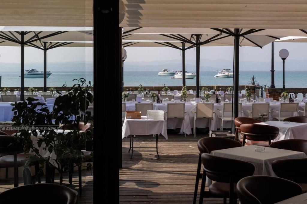 un restaurant avec des tables et des chaises blanches et l'océan dans l'établissement Villa Pioppi Hotel, à Sirmione