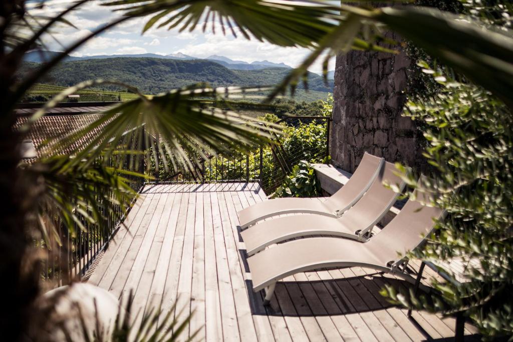 deux bancs blancs assis sur une terrasse en bois avec un arbre dans l'établissement Romantik Hotel Jagdhof, à Caldaro