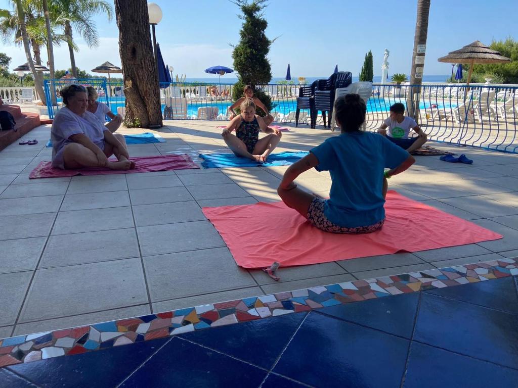 un groupe de personnes assises sur des tapis près d'une piscine dans l'établissement RESIDENCE EMARINE con SERVIZIO SPIAGGIA INCLUSO, à Peschici