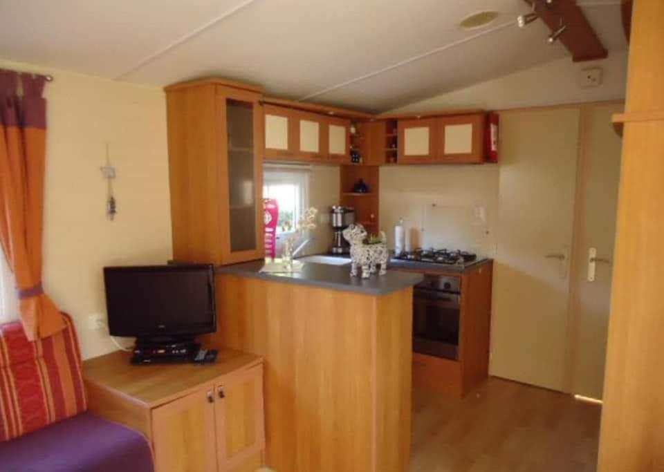 Il comprend une cuisine avec des placards en bois et une télévision. dans l'établissement Mobil-home, à Pont-Aven