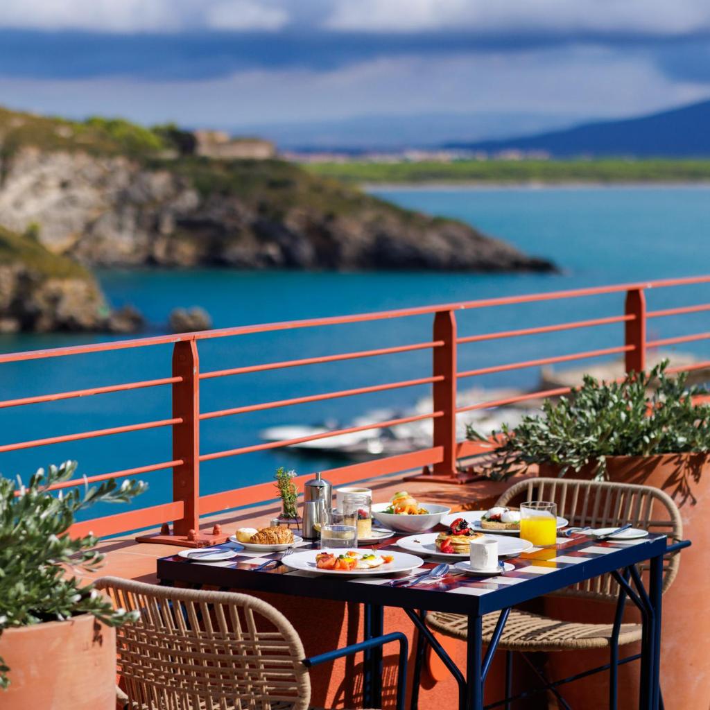 une table avec de la nourriture sur un balcon avec vue sur l'océan dans l'établissement La Roqqa, à Porto Ercole