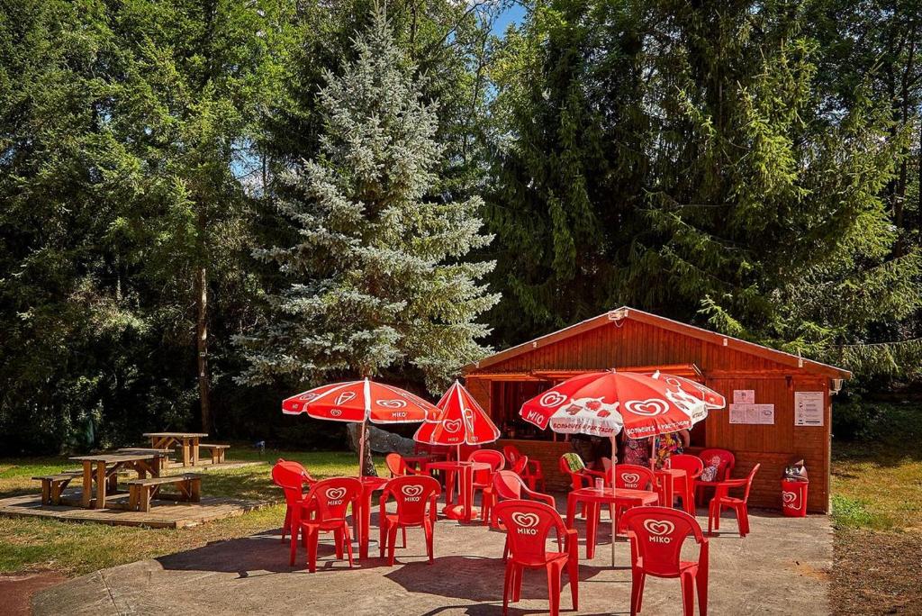 un groupe de chaises rouges, de tables et de parasols dans l'établissement location mobil-home le parc des roches, à Saint-Chéron