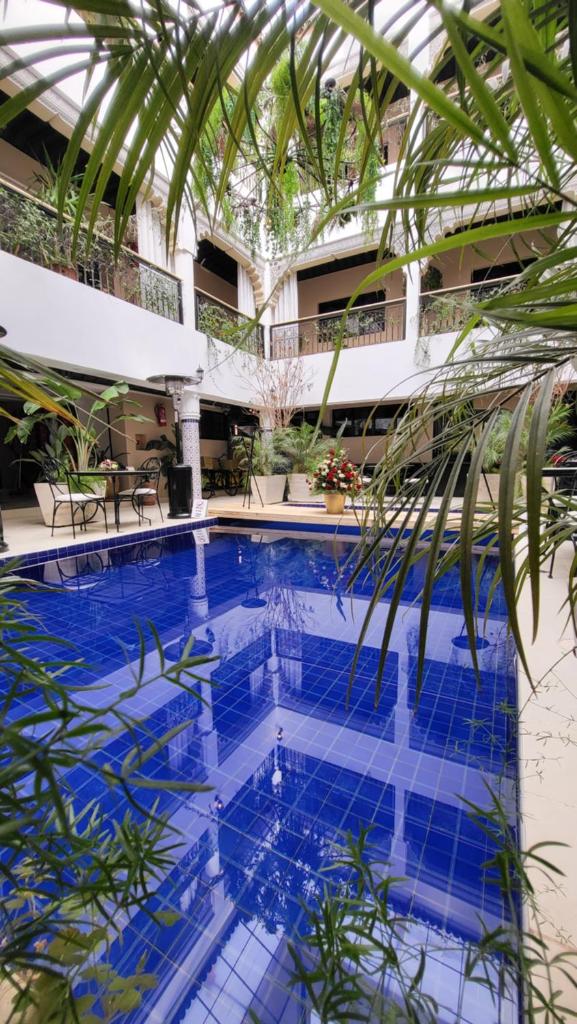 une grande piscine avec un palmier en face d'un bâtiment dans l'établissement Riad Soir De Marrakech, à Marrakech