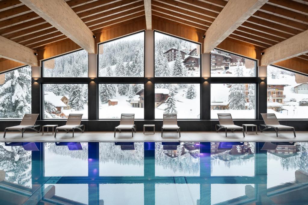 - une piscine avec des chaises et des fenêtres dans l'établissement MGM Hôtels & Résidences - Résidence Le Hameau de l'Ours, à Manigod