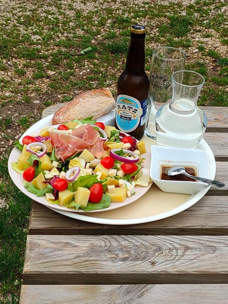 - une assiette de nourriture avec une salade et une bouteille de bière dans l'établissement CAMPING LE BEL AIR tente insolite Sibley's 4 personnes-LE ROMARIN, à Limogne-en-Quercy