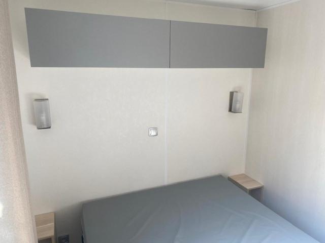 Cette chambre blanche dispose d'un lit avec deux lumières sur le mur. dans l'établissement Mobil home 456, à Ivry-la-Bataille 3 autres photos
