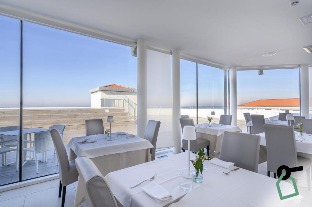 un restaurant avec des tables et des chaises blanches et de grandes fenêtres dans l'établissement HOTIDAY Room Collection - Tirrenia, à Tirrenia