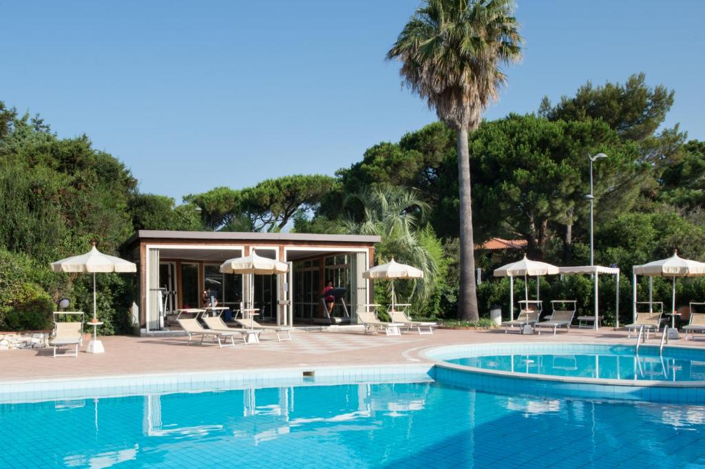 une piscine avec parasols et chaises et un palmier dans l'établissement Park Hotel Marinetta - Beach & Spa, à Marina di Bibbona