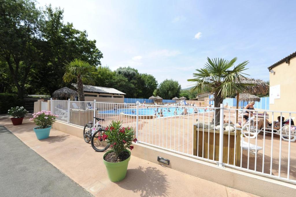 une clôture à côté d'une piscine avec un vélo dans l'établissement Mobil Home XXL 4 chambres - Camping Le Viaduc, à Millau