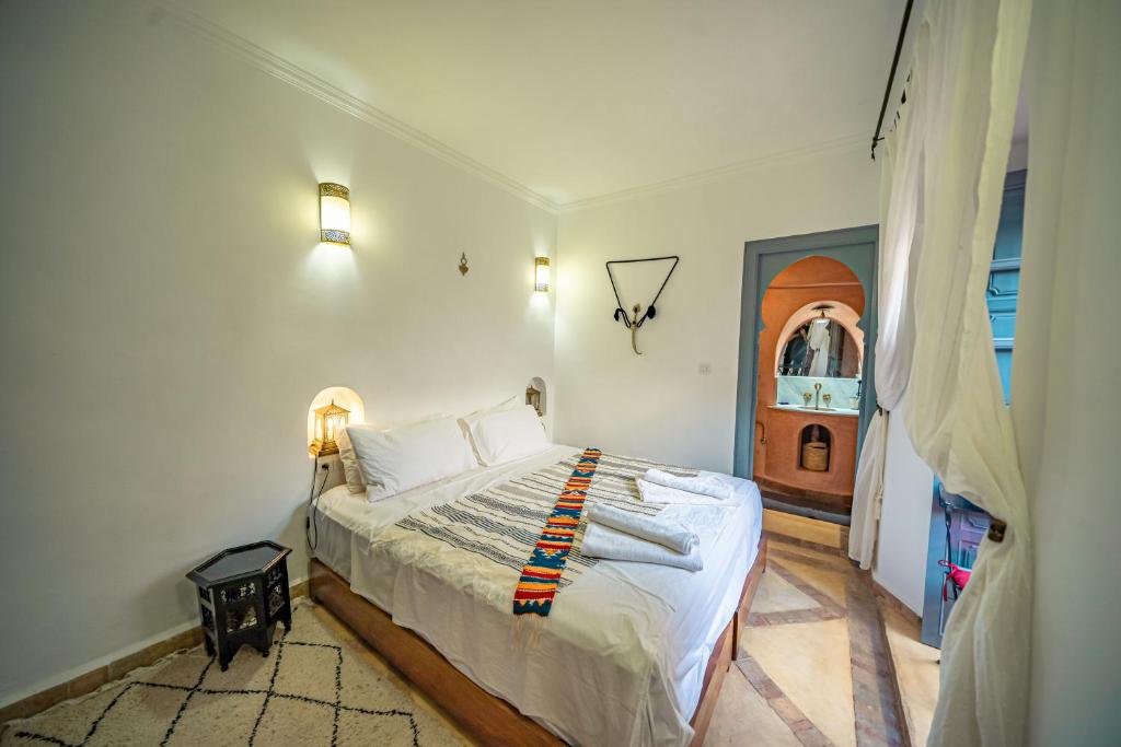 une chambre avec un lit avec des draps blancs et une porte dans l'établissement Riad Azawan, à Marrakech