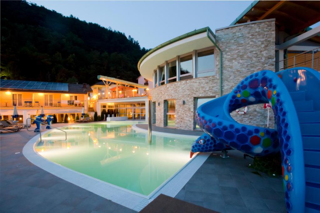 une piscine avec un toboggan bleu en face d'un bâtiment dans l'établissement Parc Hotel Du Lac, à Levico Terme
